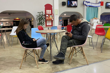 Internet addiction. Young girl and a guy are sitting at a food court table looking at their mobile phones chatting on social networks ignoring real communication. Volgodonsk, Russia October 12, 2020.のeditorial素材