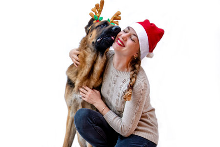 Banner. Dog with deer antlers kisses girl in Santa hat. Woman and pet celebrates new year, Christmas. Greeting card with German shepherd on white isolated background with space for text. Copy space.の写真素材