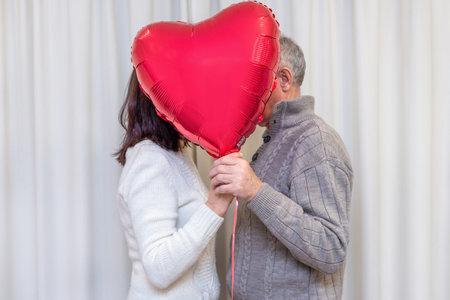 Happy couple seniors celebrate Valentines Day. Faceless couple with no face behind heart balloon. Romantic relationships, love and dating in retirement. Lifestyle of elderly people. Mature pensioners.の写真素材