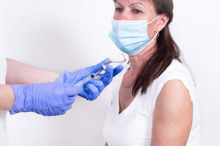 Female doctor or nurse giving shot or vaccine to patients shoulder. Vaccination and prevention...