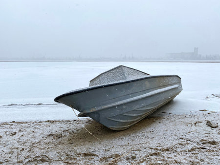 A lonely motor fishing boat is parked under the snow on the river bank. Winter parking in...