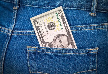 Five dollars bill sticking out of the blue jeans pocketの写真素材