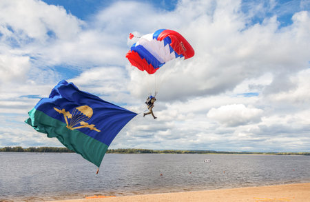SAMARA, RUSSIA - SEPTEMBER 11, 2016: Single military parachute jumper on a  wing parachute execute a controlled descent by parachute hung with airborne flagのeditorial素材