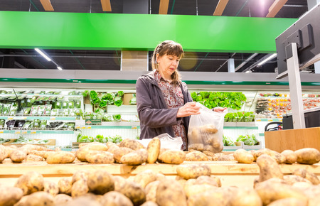 Samara, Russia - September 5, 2017: Young woman choosing fresh potatoes at shopping in supermarketのeditorial素材