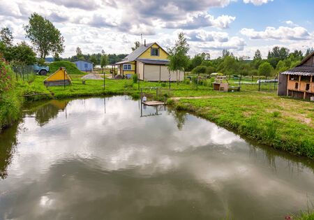 Wooden village house with outbuildings and small pond in summertimeのeditorial素材