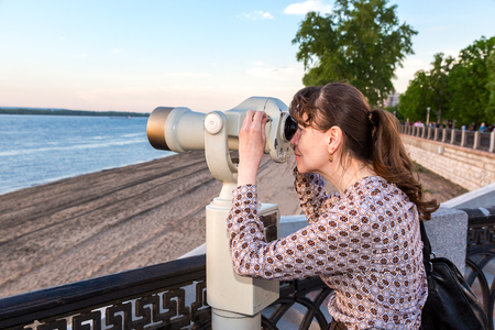 Samara, Russia - May 19, 2018: Young woman looking through the coin operated binocular on the bank of river Volga in summertimeのeditorial素材