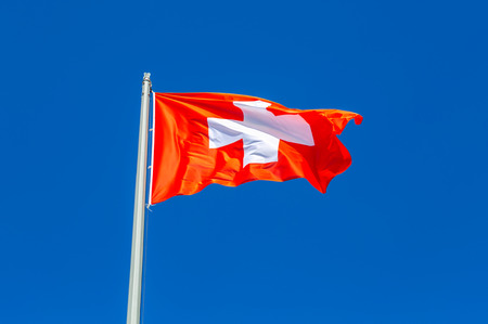 Flag of Switzerland flying in the wind against the blue skyの写真素材