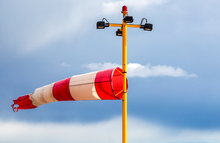 Horizontally flying windsock wind vane with red and white lines against blue skyの写真素材