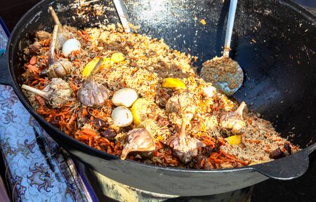 Appetizing traditional Uzbek pilaf with vegetables in a large cauldron outdoorsの写真素材