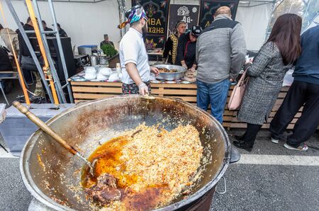 Samara, Russia - October 5, 2019: Cooking appetizing traditional oriental pilaf in a large cauldron outdoors during the holidayのeditorial素材
