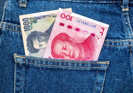Banknotes of Japanese yen and Chinese yuan sticking out of the back jeans pocketの写真素材
