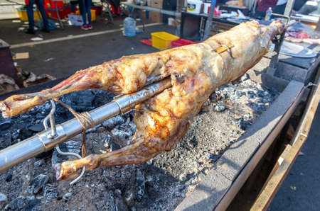 Cooking lamb carcass on a spit roasted on the open fire of the barbeque grill in the street market. Traditional Serbian roasting lamb or pork barbecueの写真素材