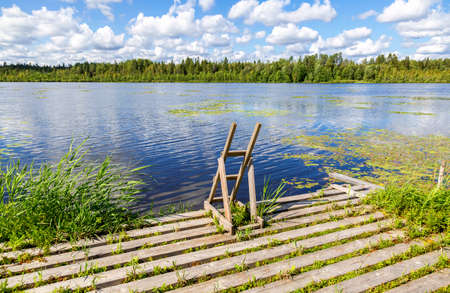 Wooden pier and ladder allowing to enter the water on the lake in a summer sunny day. Beach pier for jumping, fishing and snorkelingの写真素材