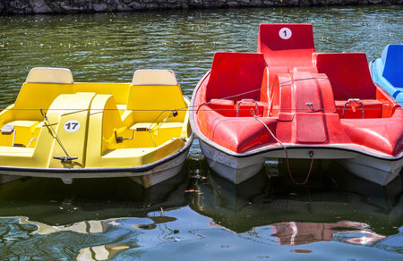 Some colorful plastic catamarans are in a row on the water surface of city pond. Summer vacation on...