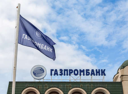 Samara, Russia - June 4, 2022: Signboard with the logo of the Gazprombank and flag against the blue sky. Text in english: Gazprombankのeditorial素材