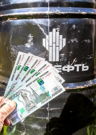 Samara, Russia - August 08, 2022: Barrel of Rosneft motor oil with brand logo and russian roubles in the handのeditorial素材