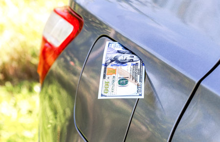 One hundred american dollar banknote sticking out of the gas tank of a vehicle. fuel economy concept...