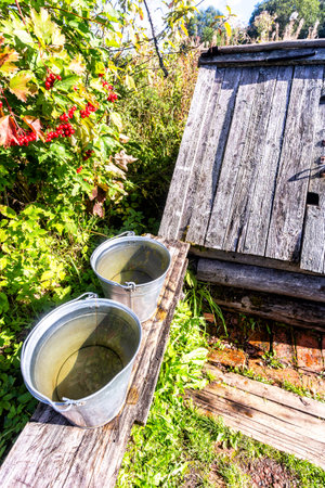 Metal buckets with water on a bench near a village wooden well on a sunny day at the countrysideの写真素材