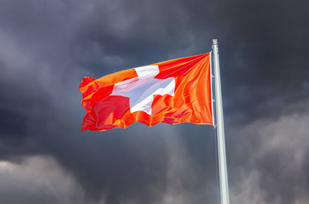 Flag of Switzerland flying in the wind against a dark sky. Switzerland national flag waving in the dark cloudy skyの写真素材