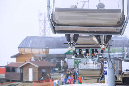 Skiers riding on a cableway chair ski lift in the fog at winter scenic close upの写真素材