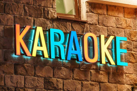 Colorful neon illuminated Karaoke sign on stone building wall background. Architectural decor of entertainment facilities.の写真素材