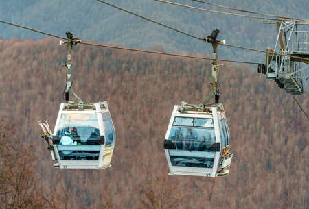 Sochi, Russia - January 7, 2018: Two gondola cabins of Gorky Gorod cable way ski lift full of skiers on bare forest mountain background. Close up view.のeditorial素材