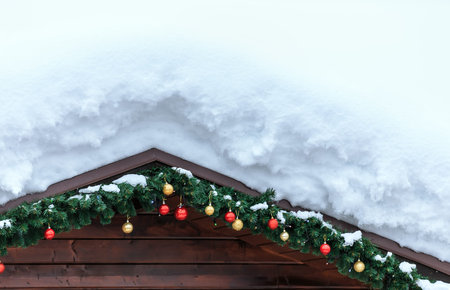Snow covered wooden roof with hanging spruce branches and colorful new year Christmas toys and...