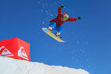 Sochi, Russia - March 25, 2014: Man snowboarder flies in the air from a jump on blue sky and mountain rock background at winterのeditorial素材