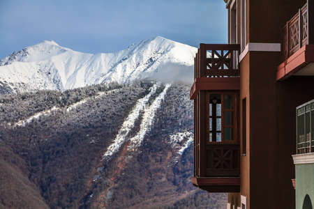 Scenic winter view of Gorki Hotel exterior on snowy Caucasus mountain peaks and blue sky background at Gorky Gorod ski resort in Sochi, Russia - Russian landmark for holiday and vacation.のeditorial素材