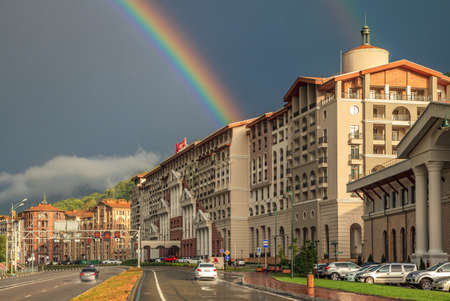 Sochi, Russia - August 24, 2015: Summer sunny cityscape of modern Marriott Hotel building in Gorky Gorod mountain ski resort. Scenic landscape with double rainbow, sun shower and cars on the roadのeditorial素材