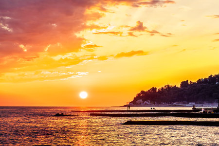 Golden sunset with distant spurdikes on Black Sea coast in Khosta, Sochi, Russia. Beautiful scenic summer seascape.の写真素材