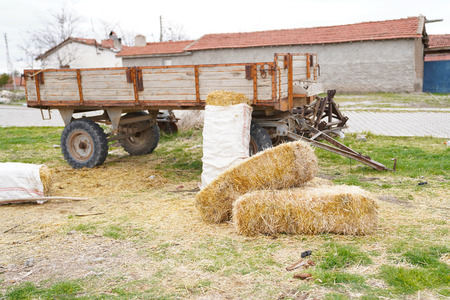 Several hay bales next to the tractor trailer and country houses and hayloft in backgroundの写真素材