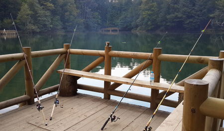 Fishing rods leaning against the hand rail on a wooden marine jetty or pier with no fishermanの写真素材