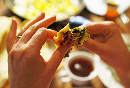 Woman eating gozleme with spinach and  blurred teacup and other foods in backgroundの写真素材