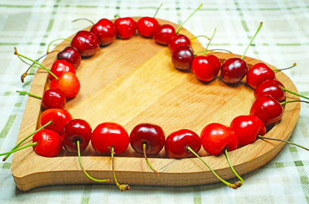 Sweet cherry berries in heart-shaped wooden bowl in a rowの写真素材