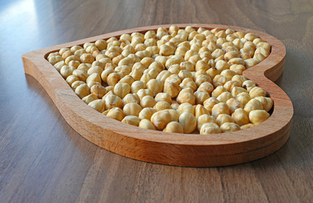 Hazelnut in heart-shaped wooden bowl on wooden tableの写真素材