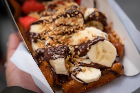 Hand holding homemade Belgian waffles with honey, banana, strawberry and chocolate backgroundの写真素材