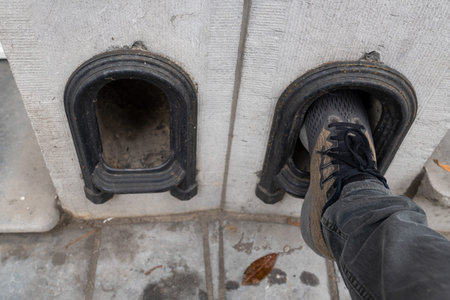 Man clean his shoes on boot scraper in a low wall at the entrance to the drive of a terraced house....