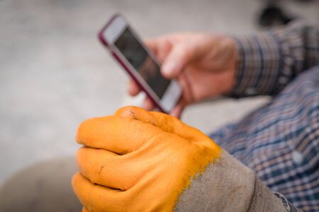 Worker wearing yellow gloves is looking on mobile during breakの写真素材