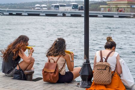 Istanbul, Turkey- August 04 2019: Back view of three girls eating boiled corn near sea,の写真素材