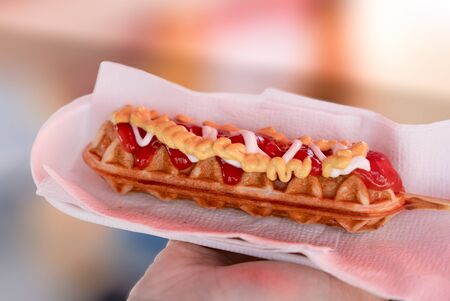 Hot dog waffle on a stick is on a man's hand. Hot dog waffle is ready to eat.の写真素材
