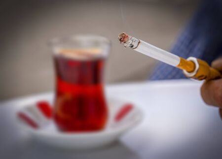 The hands of male holding cigarette with an holder and blurred turkish tea on the table. Selective focus.の写真素材
