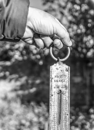 Hand holding retro pocket spring balance in a farm or field in black and white