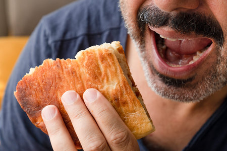 Mustachioed man holds bread and is ready to bite bread. Man opens mouth to eat bread.