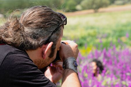 Long haired male photographer takes a photo of a girl in purple flowersの写真素材