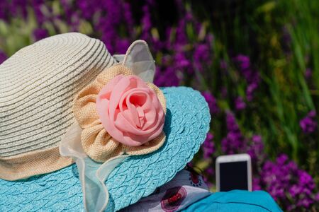 Back view of woman in a straw hat with a flower pattern is looking at the mobile phone in flowersの写真素材