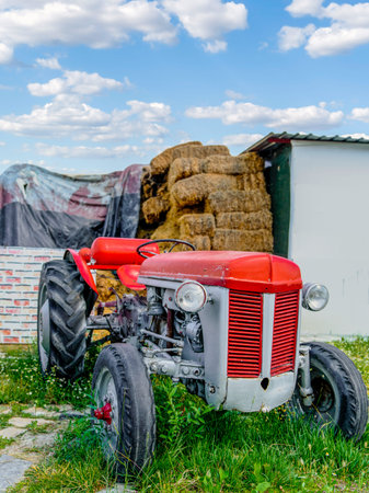 Selective focus of antique red tractor and hay bale in background. Vintage village lifestyle.