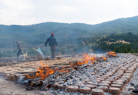 Mihaliccik, Eskisehir/Turkey-July 26 2020: Male worker throws wood on fire to dry clay pots.のeditorial素材