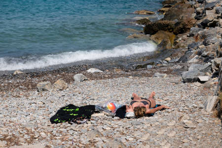 Unidentified woman sunbathing on pebbles by the sea.の写真素材