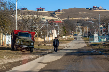 Shamakhi, Azerbaijan - January 07 2022- Old molokan people walking on the road and an old russian truck is parked by the roadside with a hill in background.のeditorial素材